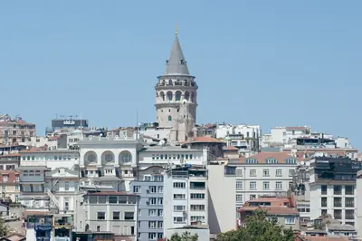 A daytime view of the iconic Galata Tower surrounded by Istanbul's urban landscape.